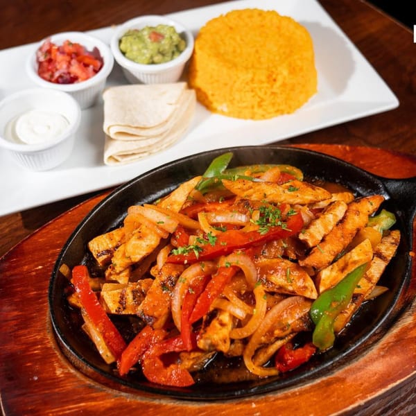 Sizzling chicken fajitas with peppers and onions, served with rice, guacamole, salsa, and tortillas.