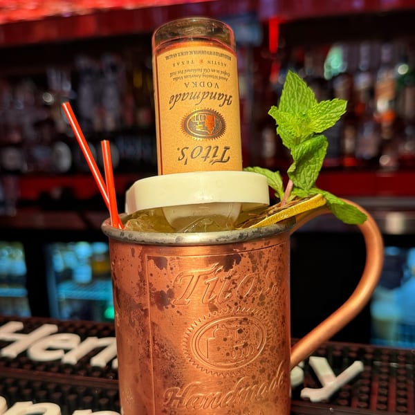 A Tito's Handmade Vodka bottle inverted into a copper mug with a cocktail, mint, and lime.