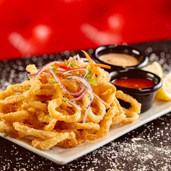 Crispy fried calamari rings with colorful vegetable garnish, two dipping sauces, and lemon wedges.