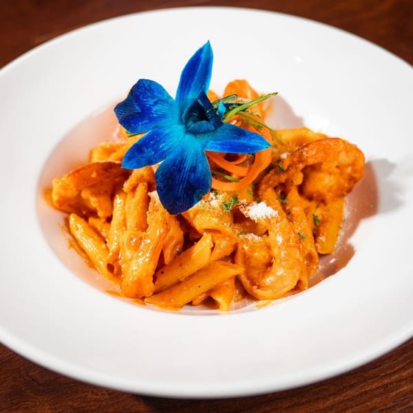 Penne pasta with shrimp in a creamy orange sauce, garnished with a vibrant blue orchid.