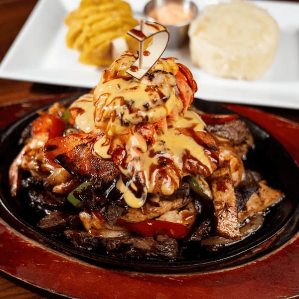 Sizzling fajitas with shrimp, chicken, and steak, topped with melted cheese and a "2" pick.