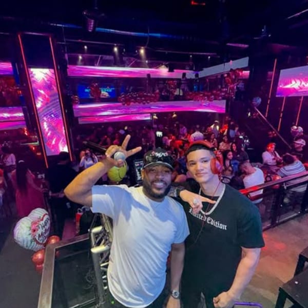 Two men posing for a photo in a vibrant, neon-lit Boca Restaurant Lounge with a crowd.