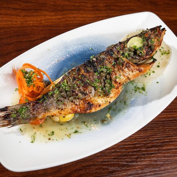 Whole grilled fish with capers, herbs, and lemon, served with mashed potatoes and carrot ribbons.