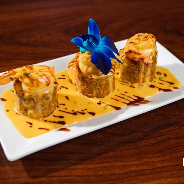 Three Latin-American shrimp dishes with yellow sauce and dark drizzles, one garnished with a blue orchid.