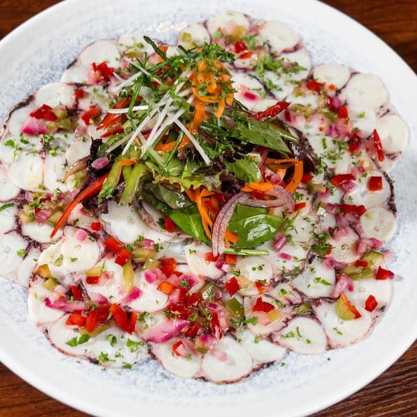 Octopus carpaccio with mixed greens, red peppers, and onions on a white plate at Boca Restaurant Lounge.
