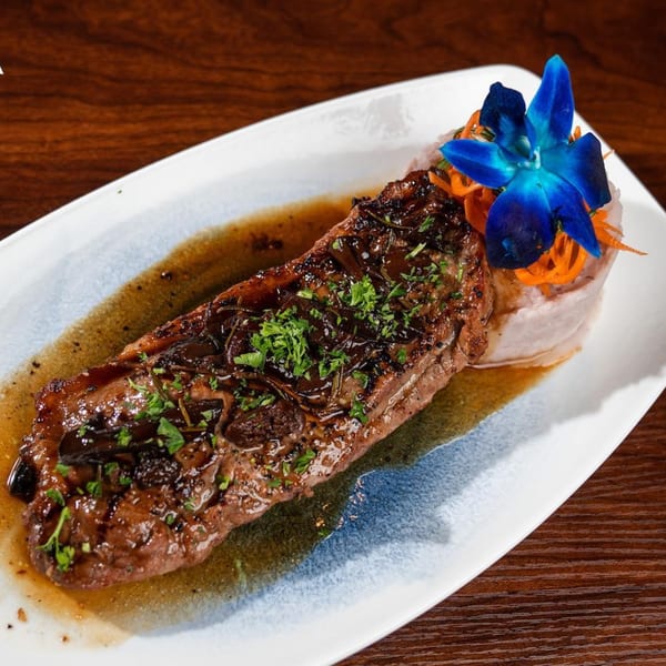 Grilled steak with sauce and herbs, garnished with a blue orchid and shredded carrots.