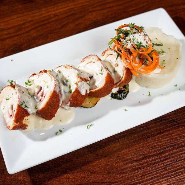 Sliced chicken cordon bleu with cream sauce, mashed potatoes, and carrot garnish on a white plate.