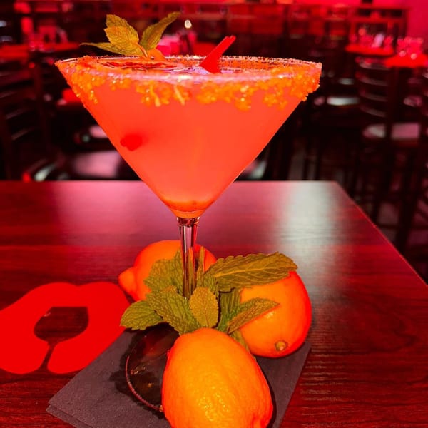Pink martini with a sugared rim, mint, and cherry, surrounded by lemons on a dark table.